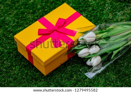 Beautiful yellow gift box with pink bow and tulips on green grass lawn