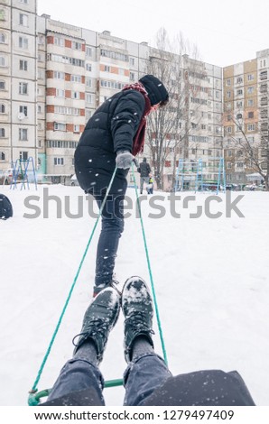 Winter season, snowing outside. Riding the sledge concept. The man is pulling sled behind himself. The photo is made from the back view by a person sitting on the sled. Follow me.