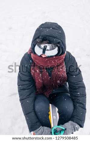 Winter season, snowing outside. Close up of a man in ski goggles and red scarf. Hair and clothes covered with snow. Top view shot. Riding the sled concept.