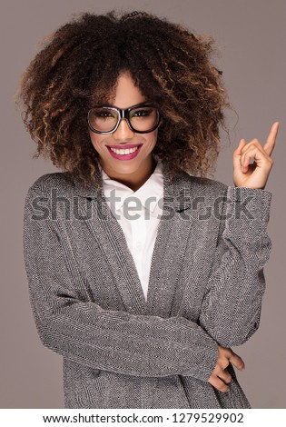 Photo of young african cheerful business woman standing over gray background , smiling to the camera.Girl with afro hairstyle .