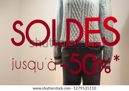 closeup of discount sign "SOLDES jusqu'a 50%" in french,  the traduction of  (sales until 50%) on window in french fashion store showroom on winter clothes background