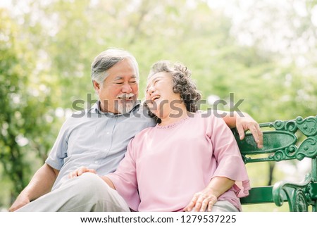 Happy Asian Senior couple laughing while sitting on the bench in the park  Royalty-Free Stock Photo #1279537225