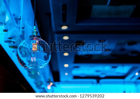A cool retro style lightbulb with blurred bottles in the background illuminated by a soft blue light