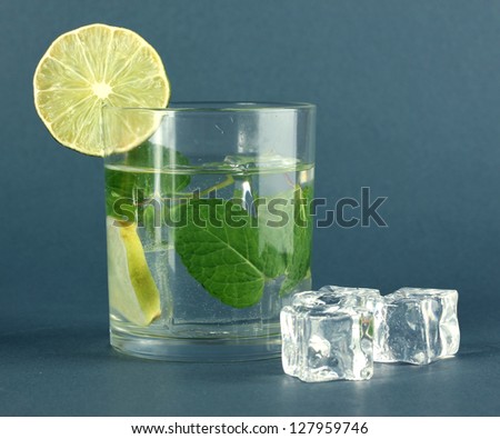 Glass of water with ice, mint and lime on grey background