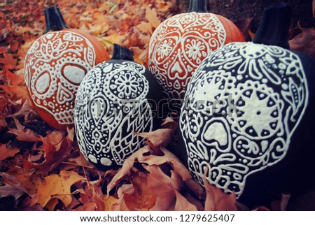 Seasonal Halloween painted pumpkins with sugar skull face artwork sit in orange autumn leaves. The pumpkins are beautiful and decorative, perfect for the spooky event.