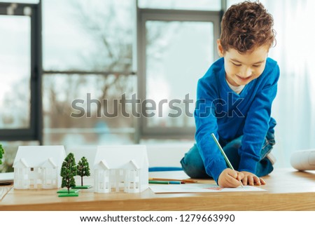 Drawing pictures. Positive little boy smiling while sitting on the table and smiling