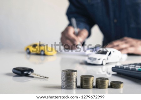 Businessman are saint documents about cars  with  some coins calculator and car toy on desk.
