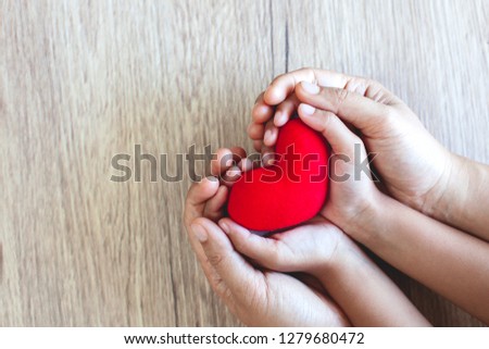 Red heart in child hands and parent hands on wooden table background with love and harmony