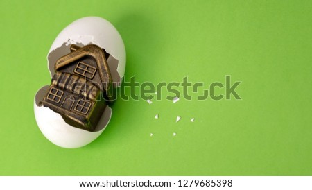 Souvenir toy building in a broken egg on a green background. White eggshell with a golden gift instead of yolk inside. Concept happy birthday new home. Mortgage or loan for housing. Copy space.