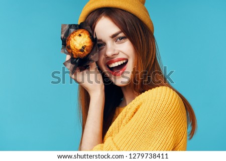 A happy woman has a dazzling smile. Look around in a hat holding a fresh cupcake in the face                         