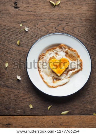 Top view of heart yolk sunny side up on plate on wood table with small leaf and flower decoration. Sweet Breakfast for special day like Valentine's day, Anniversary, Date or birthday