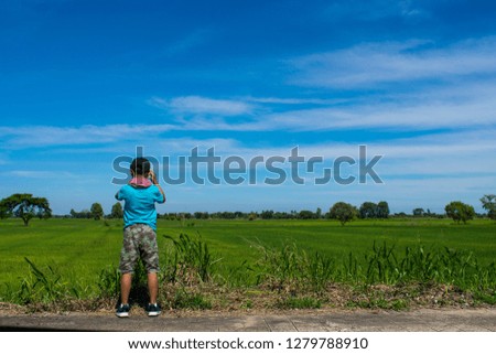 A child boy with camera taking pictures at the side road on summer day among green trees and light sky background.