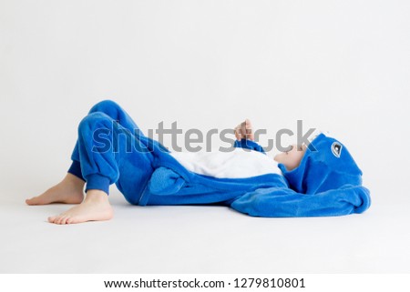 cheerful little boy posing on a white background in pajamas, blue shark costume