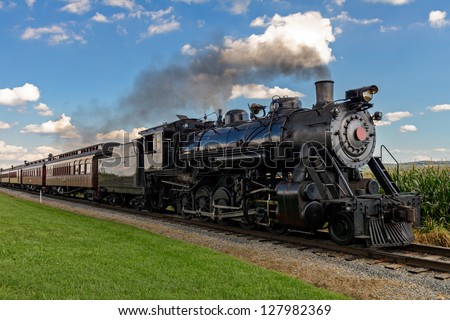 historic steam train passes through the fields Royalty-Free Stock Photo #127982369