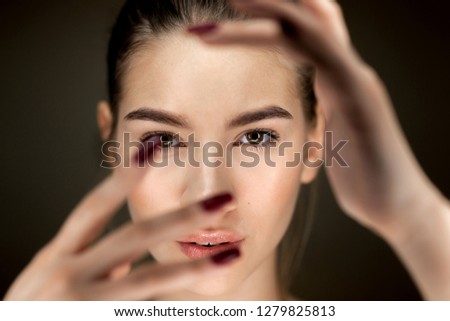 Portrait of young beautiful brown-haired girl with natural makeup holding her fingers in front of her face