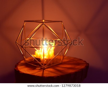 Warm light of hand made natural bee wax dying candle in the golden metal candle holder on wooden slice. Cozy interior detail in modern style. 