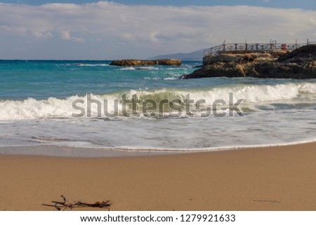 Focus on a incoming wave with a sandy beach in foreground and cliffs and cloudy sky in background, picture from Crete Island Greece,Limenas Chersonisou. 