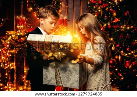 A portrait of children opening a gift box. Merry Christmas, happy New Year. Luxurious apartment with christmas lights and decorations. Miracle time.