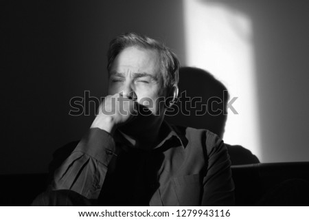 Man depressed in shadows with hand on head