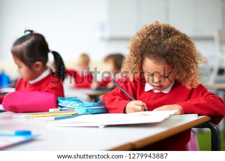 Schoolgirl sitting at a desk in an infant school classroom drawing, close up Royalty-Free Stock Photo #1279943887