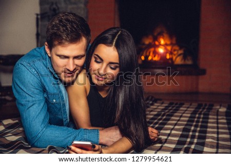 Wonderful picture of young people in love. He embrace her. They keep eyes closed. Couple lying not far from fireplace.