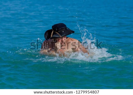 Emotional man in a black hat pirate posing in the surf in the water on the beach.