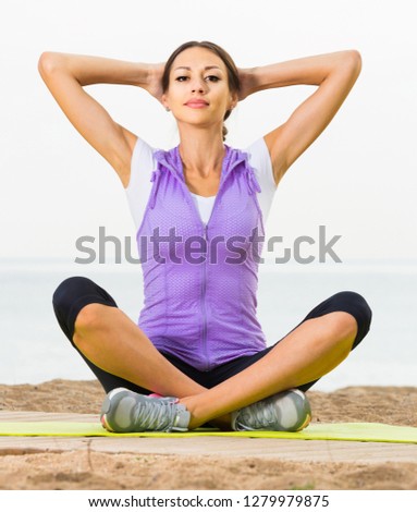 Smiling girl doing youga training cross-legged on beach on  sunny day