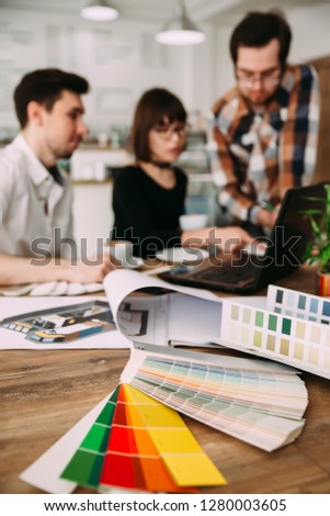 Group of young architects working on a new project, selective focus in the foreground on the drawings and color tables, background image