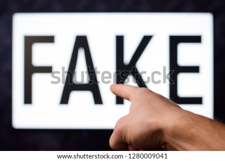 Hand points to a screen with inscription FAKE. Symbol of false, untruth, disinformation