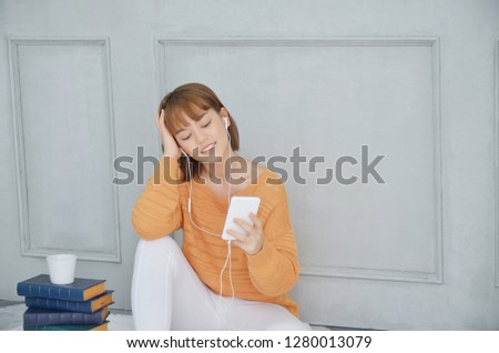 Woman smiling.Beautiful Asian women wearing orange shirts listening to happy music in the morning room.Do not focus on the object.
