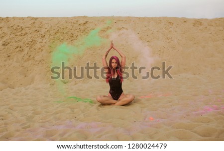 Gorgeous brunette woman with long hair posing with a cloud of Holi paint, sitting on the sand