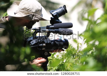 Photographer or videographer holding the video camera on a tripod on top of the mountain. Forest,ocean and blue sky  background.