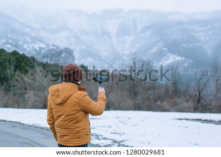 Tourist in a yellow jacket and jeans  photographed mountains  in the new generation smart phone with snowy background in winter time. 