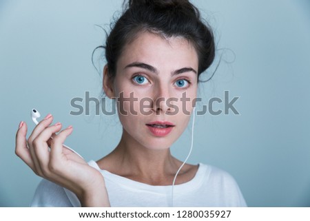 Close up of a beautiful young casual girl standing isolated over blue background, listening to music with earphones