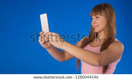 a girl is holding a phone in her hands, a girl with a lovely smile is holding a phone in her hands, a girl is taking pictures of herself on the phone