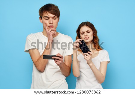 A man and a woman in white T-shirts are standing nearby and are looking into the phone on a blue background                      