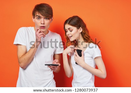 Man and woman with a phone in their hands in white T-shirts on an orange background       