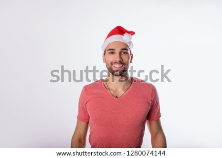 Portrait of a happy smiling bearded man in casual pink shirt and Canta Clause hat looking in camera while standing isolated in studio against white background with copy space for promotional content