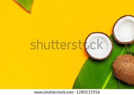 Ripe coconut and tropical leaves on yellow colored background, minimal flat lay style top view. Pop art design, creative summer and food concept. Tropical fruit whole and half abstract background