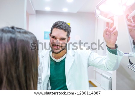 Portrait of a friendly dentist holding light in dental clinic. A young male dentist and a patient. Dentist office lifestyle scene. Doctor practice. Patient health care