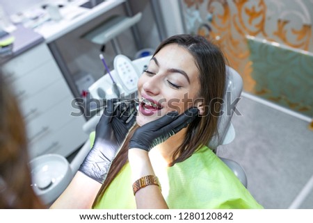 Putting dental braces to the woman's teeth at the dental office. Dentist examine female patient with braces in denal office. Close-up of a young attractive girl with braces on the teeth