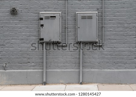 Electrical Boxes painted grey on a painted grey brick wall