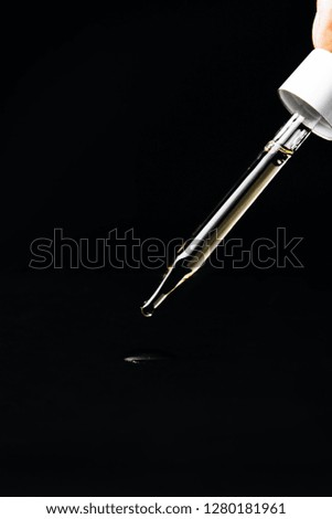 a drop of oil falling from a glass pipette isolated on a black background. cosmetology, chemistry, perfumery. macro photo close up. subject photo. liquid measuring process