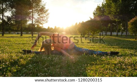 Girl gymnast sits on a string on the grass in a city park in nature and makes side bends to the legs.