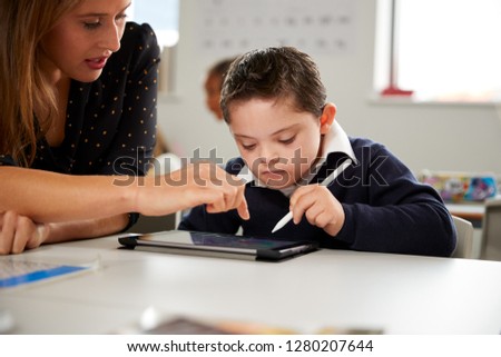 Young female teacher working with a Down syndrome schoolboy sitting at desk using a tablet computer in a primary school classroom, front view, close up Royalty-Free Stock Photo #1280207644