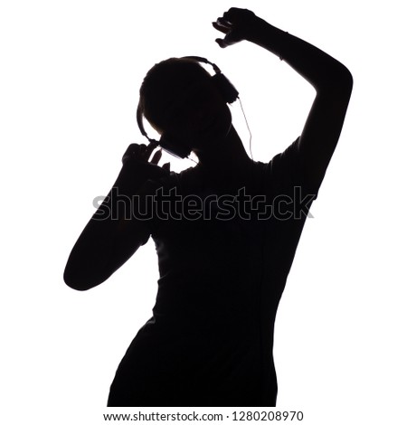 silhouette of a happy girl listening to music in headphones, figure of young woman with hands up relaxing on a white isolated background and dancing to the music, concept of hobby and leisure
