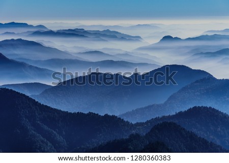 View of Himalayas mountain range with visible silhouettes through the colorful fog from Khalia top trek trail. Khalia top in himalayan region of Kumaon, Uttarakhand, India. Royalty-Free Stock Photo #1280360383