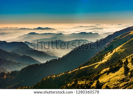 View of Himalayas mountain range with visible silhouettes through the colorful fog from Khalia top trek trail. Khalia top in himalayan region of Kumaon, Uttarakhand, India. Royalty-Free Stock Photo #1280360578