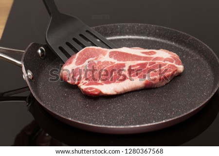 Close up picture of a beautiful raw pork steak in a non-stick frying pan on induction stove