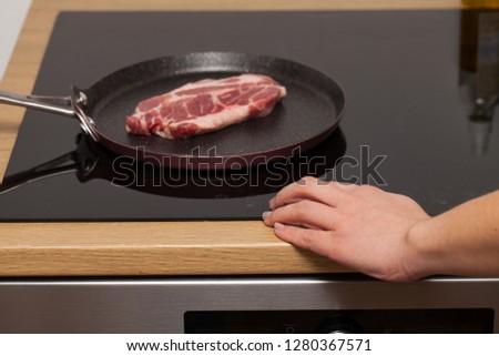 Close up picture of a beautiful raw pork steak in a non-stick frying pan on induction stove and female chefs hand